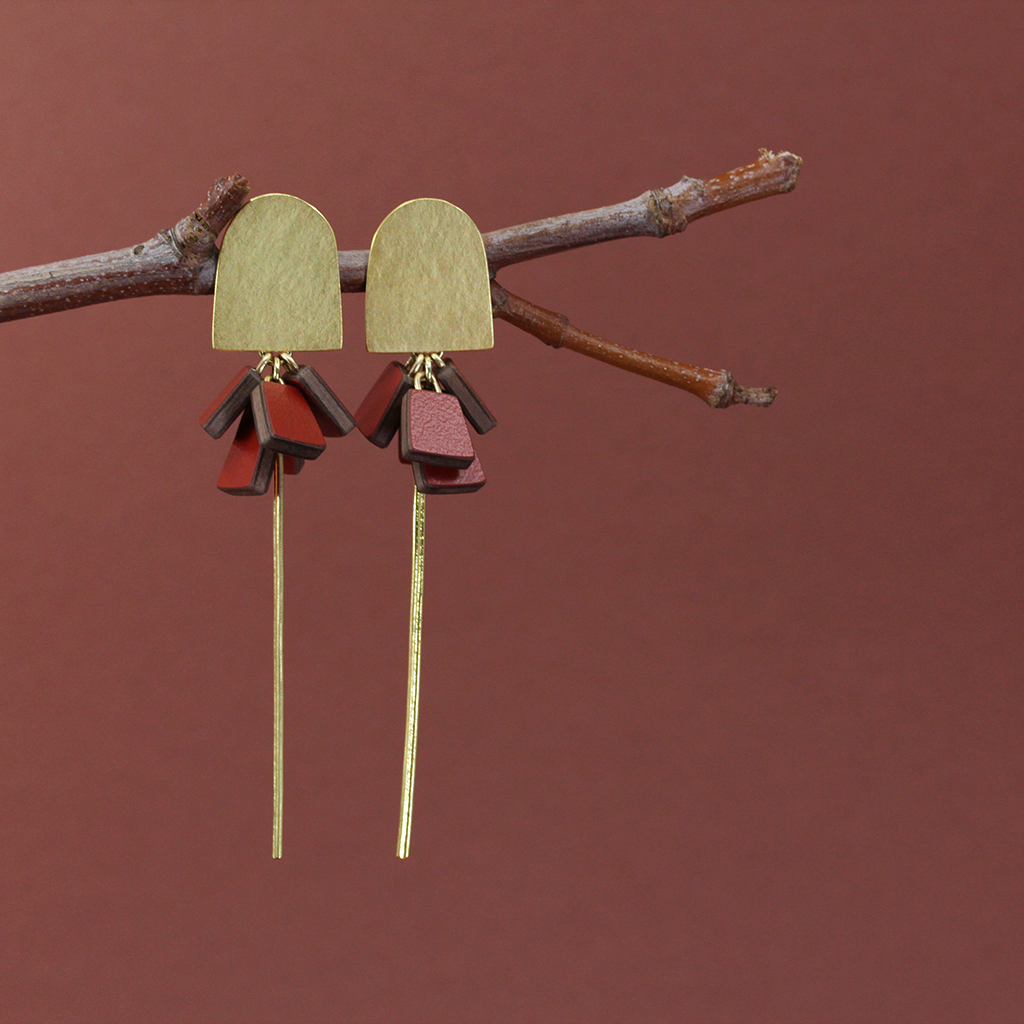 Gold arch earrings with paprika and walnut details - hanging on a branch against a terracotta background